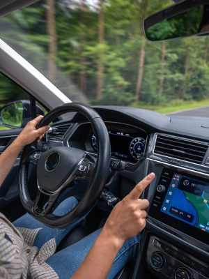 Woman driving car. Touching navigation screen. Forest road motion Vertical photo of a female driver interacting with the touchscreen navigation system while driving through a forest road with blurred trees.